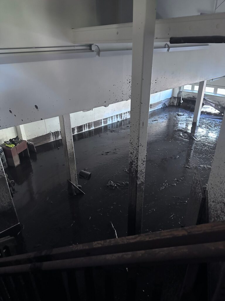 Commercial flood damage restoration in St. George, UT — silt line on the wall and standing mud across the floor after flash flooding